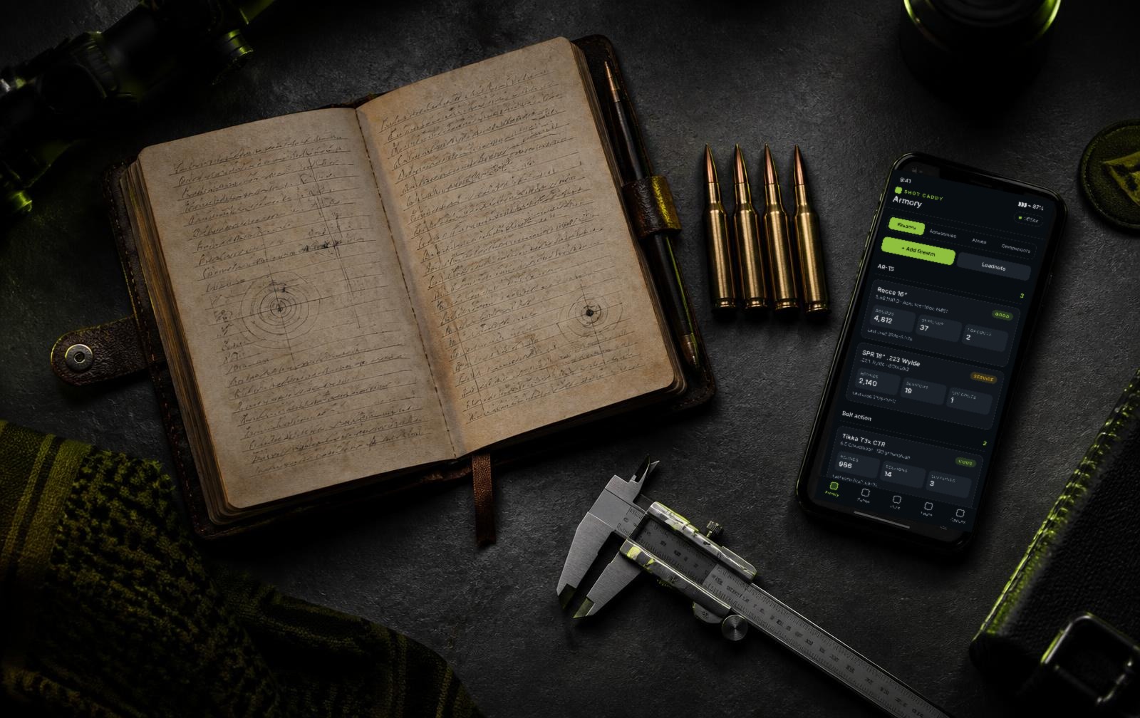 Shooting logbook, rifle cartridges and a phone showing the Shot Caddy dashboard on a dark bench